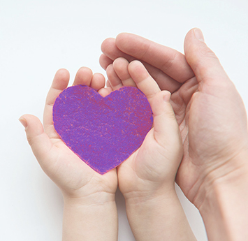 Adult hand supporting child's hands with a purple paper heart